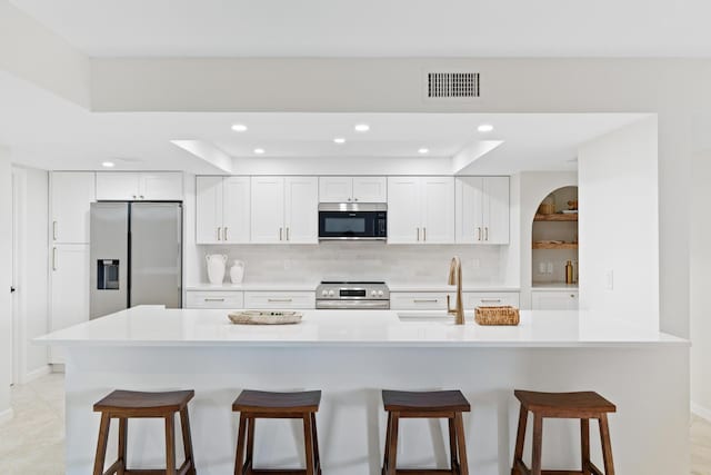 kitchen with stainless steel appliances, sink, a breakfast bar, backsplash, and white cabinets