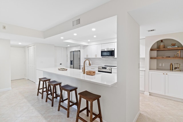 kitchen featuring white cabinetry, sink, appliances with stainless steel finishes, a kitchen bar, and light tile patterned floors