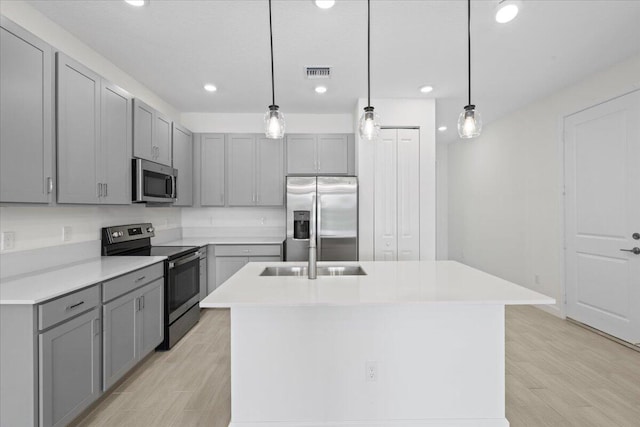 kitchen with a center island with sink, light hardwood / wood-style flooring, hanging light fixtures, and appliances with stainless steel finishes