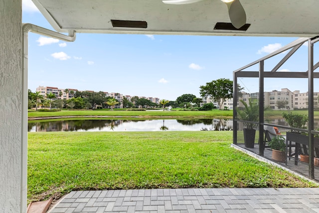 view of yard featuring glass enclosure, ceiling fan, and a water view