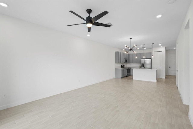 unfurnished living room featuring ceiling fan with notable chandelier and light wood-type flooring