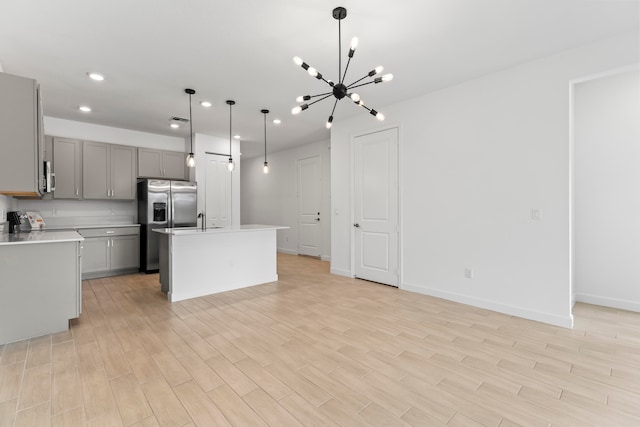 kitchen with hanging light fixtures, light hardwood / wood-style flooring, a chandelier, gray cabinets, and a kitchen island with sink