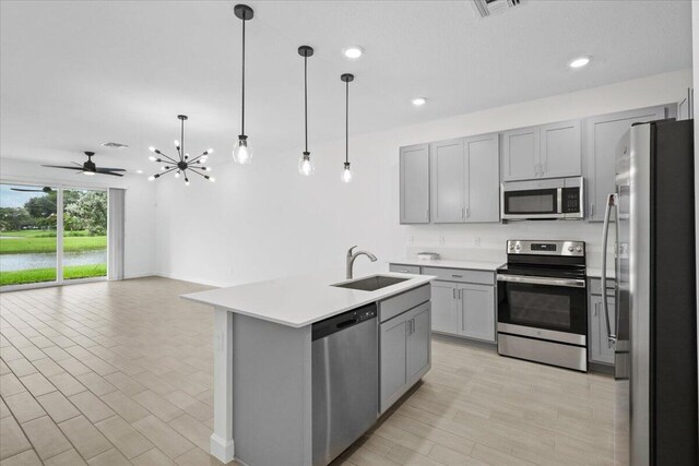 kitchen featuring gray cabinetry, sink, decorative light fixtures, a center island with sink, and appliances with stainless steel finishes