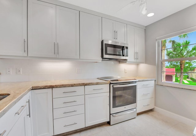 kitchen with light stone counters, light tile patterned flooring, stainless steel appliances, white cabinetry, and backsplash