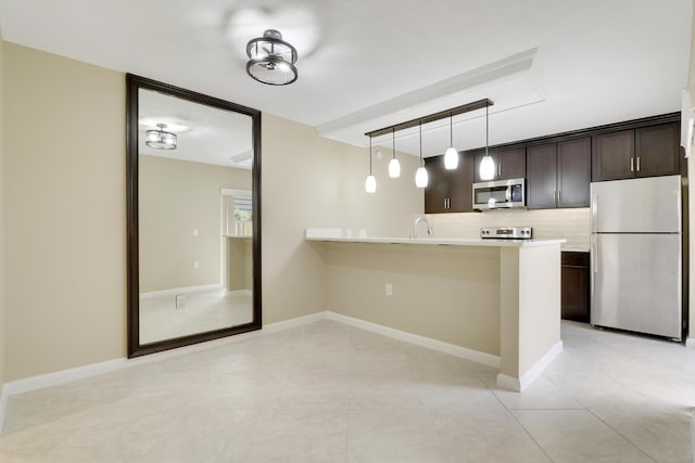 kitchen featuring kitchen peninsula, hanging light fixtures, stainless steel appliances, tasteful backsplash, and dark brown cabinetry