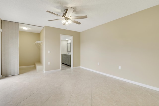 unfurnished bedroom featuring a textured ceiling, a spacious closet, light tile patterned floors, connected bathroom, and ceiling fan