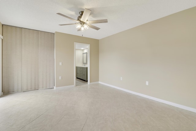 unfurnished bedroom with ensuite bathroom, a textured ceiling, ceiling fan, and light tile patterned floors