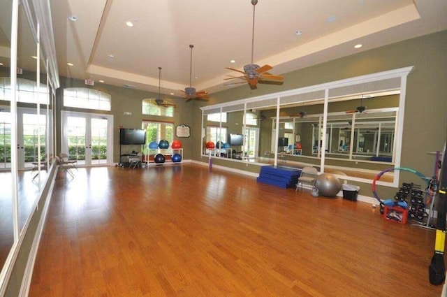 gym with a tray ceiling, french doors, ceiling fan, and wood-type flooring