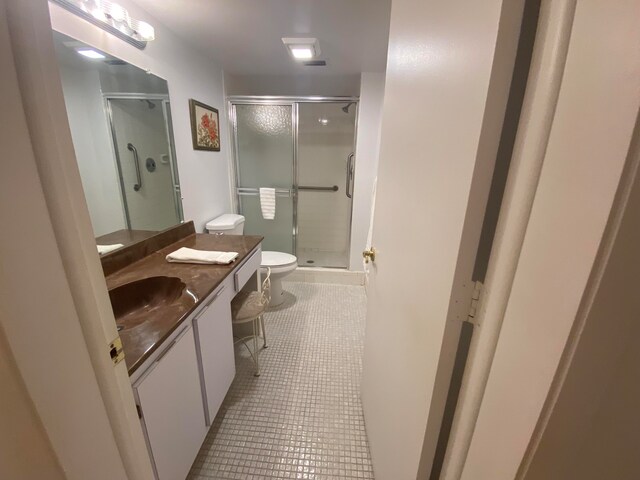 bathroom featuring toilet, vanity, tile patterned floors, and a shower with door