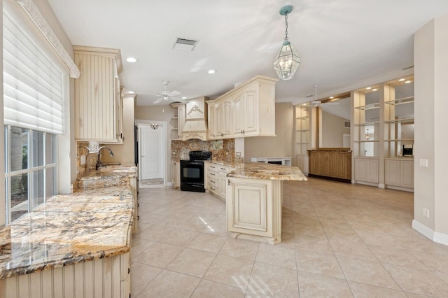 kitchen featuring light stone countertops, black range oven, cream cabinets, decorative light fixtures, and decorative backsplash