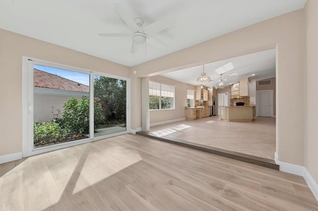 unfurnished living room featuring light hardwood / wood-style flooring and ceiling fan with notable chandelier