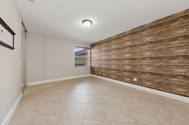 tiled empty room featuring a textured ceiling and wooden walls