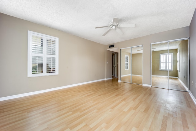 unfurnished bedroom featuring a textured ceiling, ceiling fan, light hardwood / wood-style flooring, and two closets