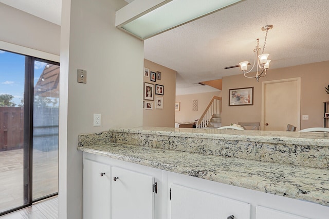 kitchen featuring white cabinetry, pendant lighting, a textured ceiling, and light stone countertops