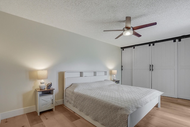 bedroom featuring a ceiling fan, baseboards, light wood-style flooring, and a textured ceiling