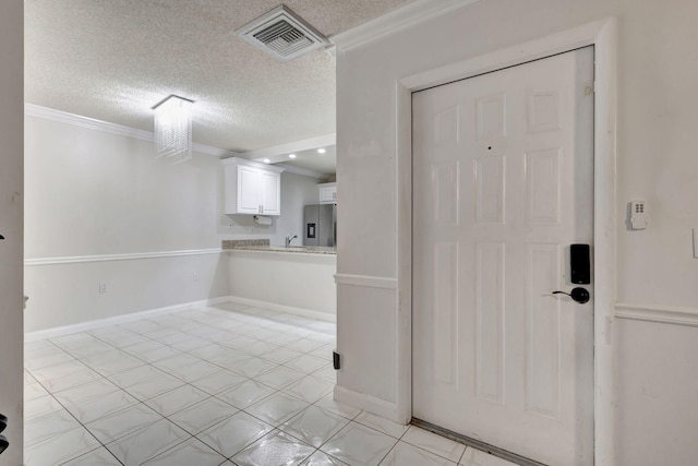 tiled foyer entrance with a textured ceiling and crown molding