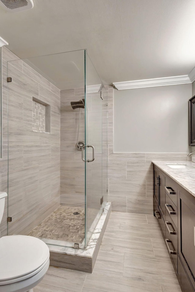 bathroom with vanity, toilet, ornamental molding, tile walls, and a shower with shower door