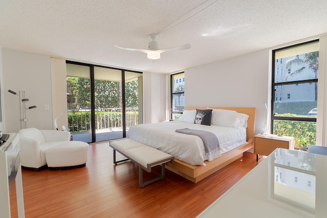 bedroom with access to exterior, a textured ceiling, ceiling fan, expansive windows, and wood-type flooring