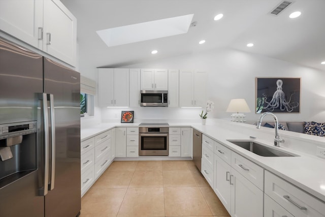 kitchen with sink, vaulted ceiling with skylight, appliances with stainless steel finishes, white cabinetry, and kitchen peninsula