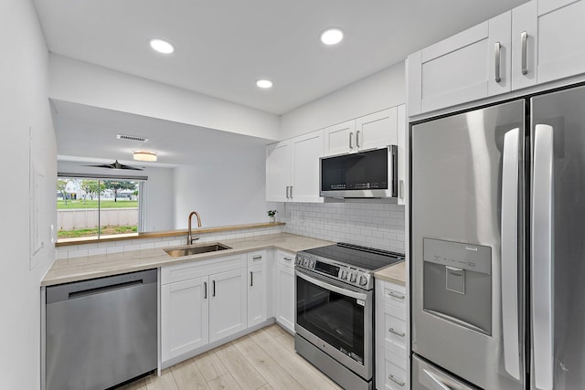 kitchen featuring backsplash, sink, appliances with stainless steel finishes, light hardwood / wood-style floors, and white cabinetry