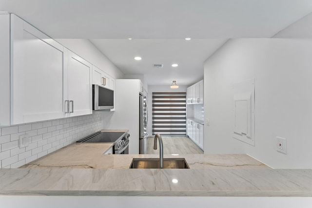 kitchen featuring backsplash, light stone counters, stainless steel appliances, sink, and white cabinetry