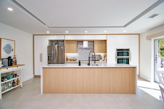 kitchen featuring sink, stainless steel appliances, white cabinetry, and wall chimney range hood