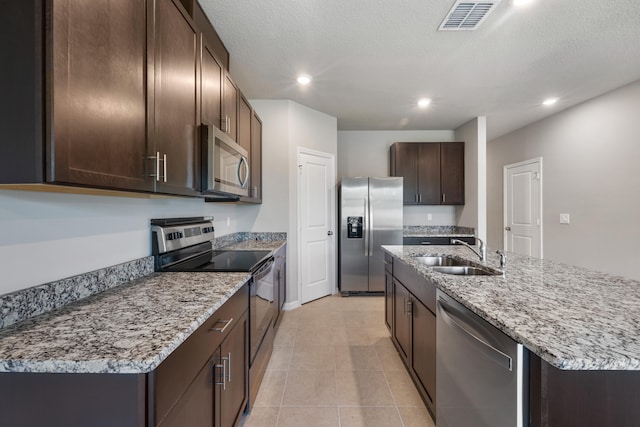 kitchen with stainless steel appliances, sink, a textured ceiling, an island with sink, and dark brown cabinets