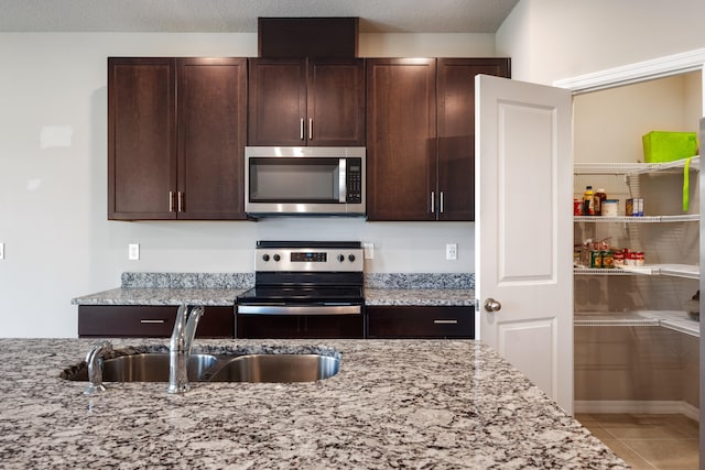 kitchen featuring tile patterned floors, appliances with stainless steel finishes, sink, and light stone counters