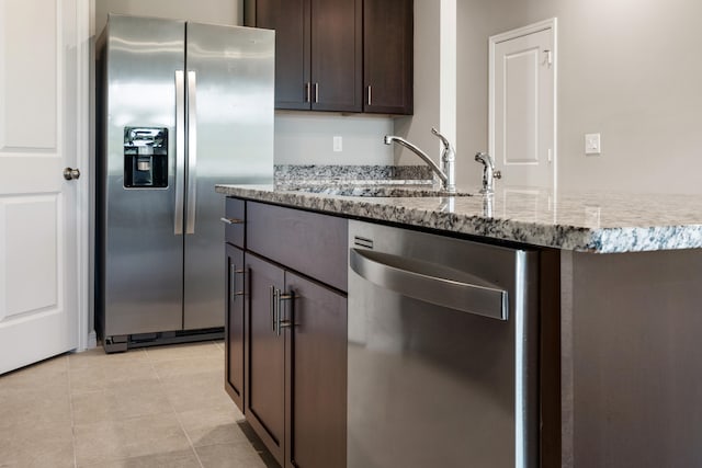 kitchen featuring light stone counters, sink, light tile patterned flooring, dark brown cabinets, and appliances with stainless steel finishes