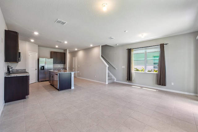 kitchen featuring appliances with stainless steel finishes, light stone counters, light tile patterned floors, and a center island