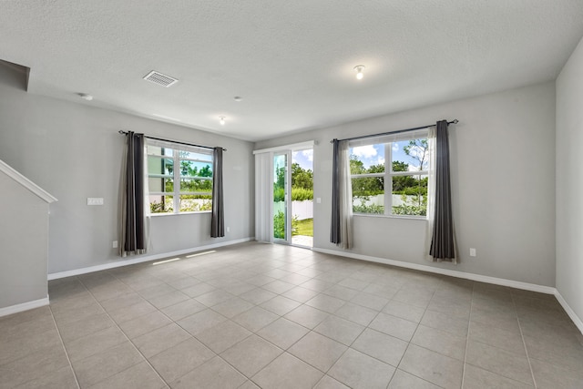 empty room with a textured ceiling, a wealth of natural light, and light tile patterned floors