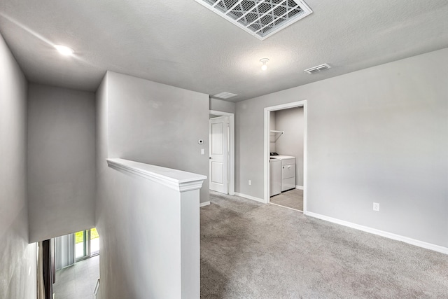 hall featuring light colored carpet, a textured ceiling, and washer and dryer