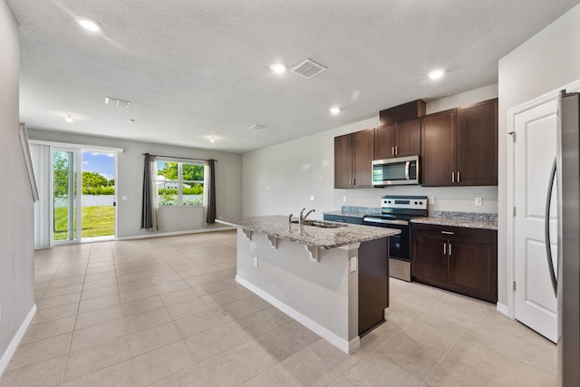 kitchen with a kitchen bar, a textured ceiling, sink, a kitchen island with sink, and appliances with stainless steel finishes