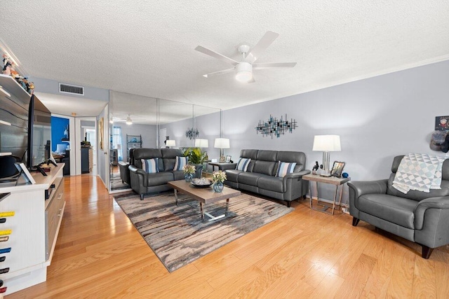 living room featuring light hardwood / wood-style floors, ceiling fan, and a textured ceiling