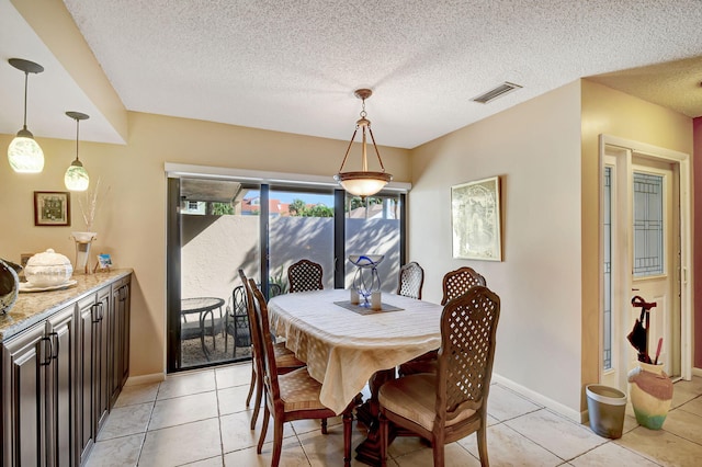 dining area with a textured ceiling, light tile patterned floors, visible vents, and baseboards