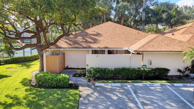 view of front facade featuring roof with shingles, fence, a front lawn, and stucco siding