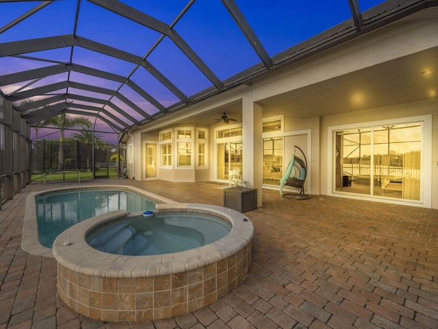 pool at dusk with ceiling fan, glass enclosure, an in ground hot tub, and a patio area