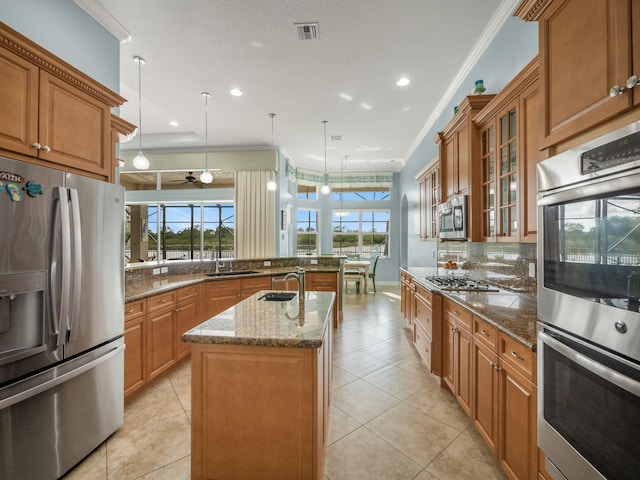 kitchen featuring stainless steel appliances, hanging light fixtures, crown molding, and an island with sink