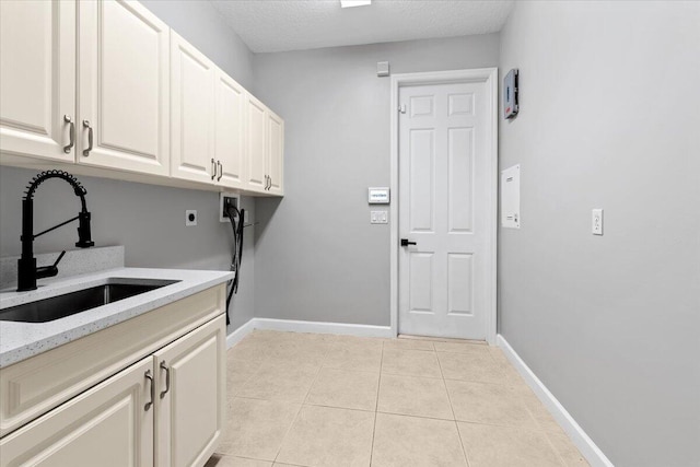 laundry area with electric dryer hookup, cabinets, sink, a textured ceiling, and light tile patterned flooring