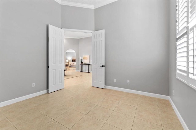 tiled spare room featuring a towering ceiling and crown molding