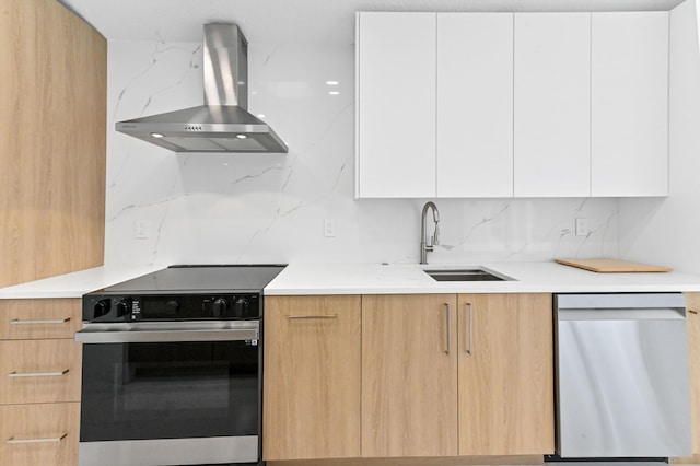 kitchen featuring tasteful backsplash, stainless steel appliances, white cabinetry, sink, and wall chimney exhaust hood