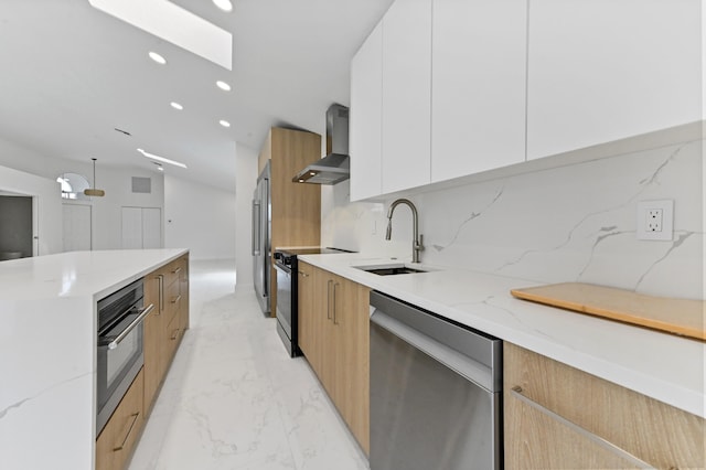 kitchen with stainless steel appliances, wall chimney range hood, light stone countertops, sink, and white cabinets