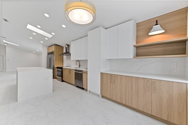 kitchen with stainless steel appliances, sink, white cabinets, wall chimney range hood, and pendant lighting