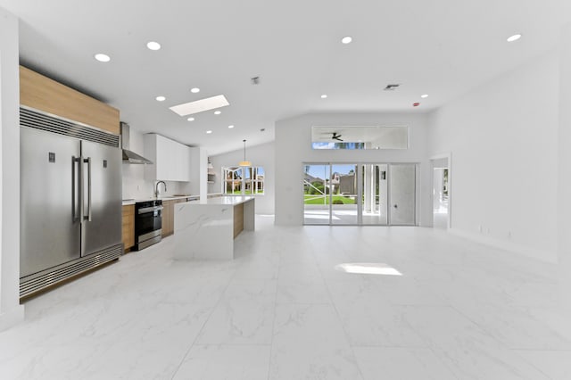 kitchen featuring appliances with stainless steel finishes, light stone countertops, hanging light fixtures, white cabinets, and wall chimney exhaust hood