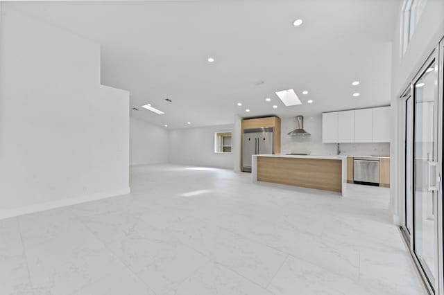 kitchen featuring white cabinets, wall chimney exhaust hood, a skylight, a kitchen island, and appliances with stainless steel finishes