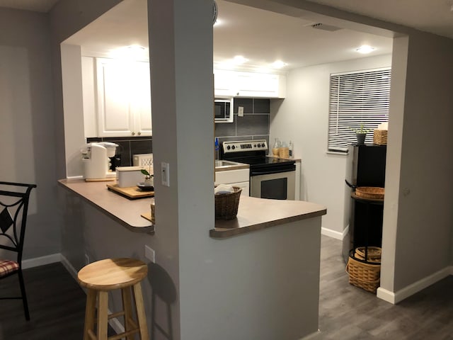 kitchen with a kitchen bar, white cabinets, decorative backsplash, hardwood / wood-style flooring, and electric range