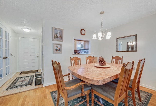 dining space with an inviting chandelier, a textured ceiling, and light wood-type flooring