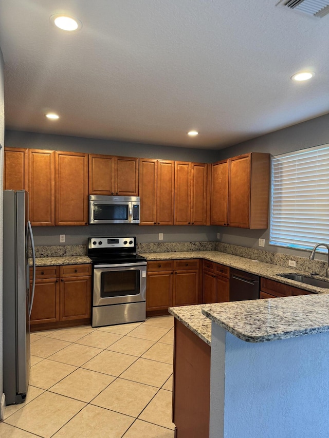 kitchen featuring appliances with stainless steel finishes, kitchen peninsula, light tile patterned floors, light stone counters, and sink