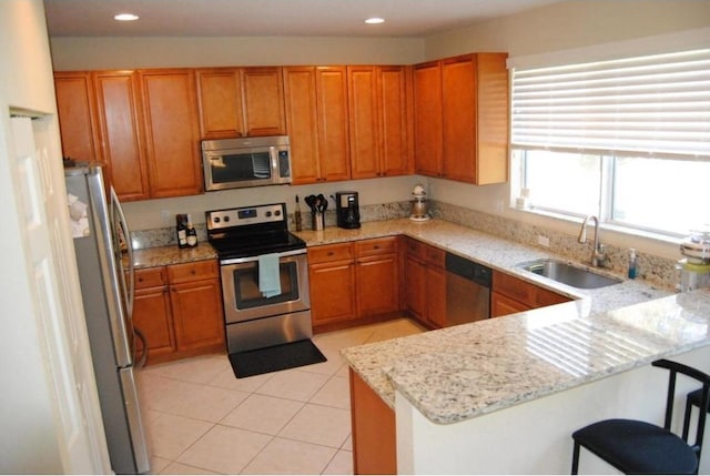 kitchen with stainless steel appliances, sink, kitchen peninsula, a breakfast bar area, and light stone countertops