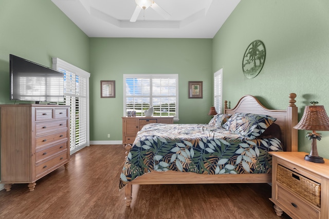 bedroom with dark wood-type flooring, ceiling fan, and a raised ceiling